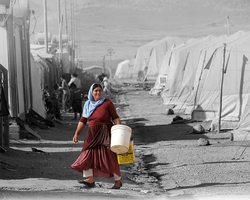 A Yazidi woman carrying a water bucked at a Yazidi refugee camp