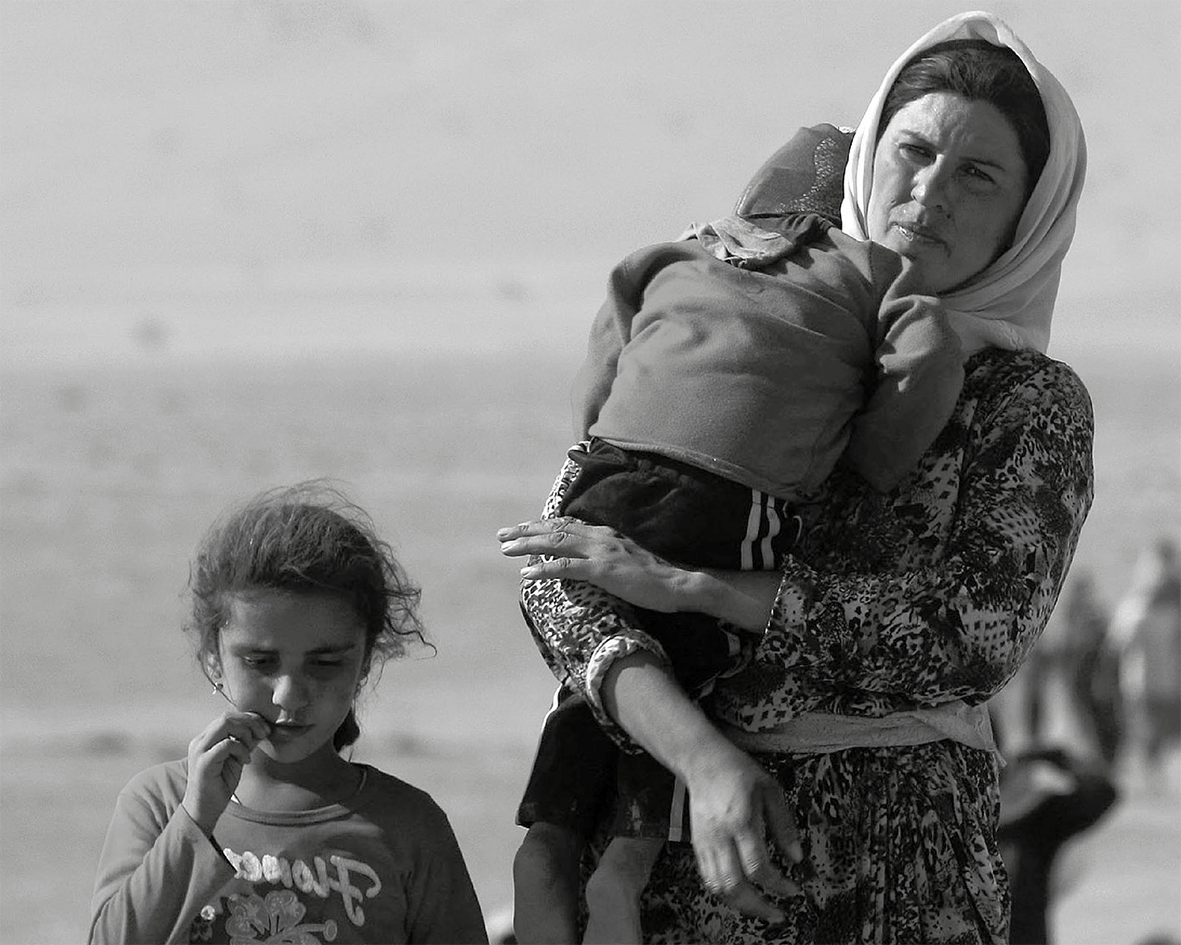 A displaced Yazidi woman carrying her child is walking with her daughter to the Syrian border, on the outskirts of Sinjar mountain