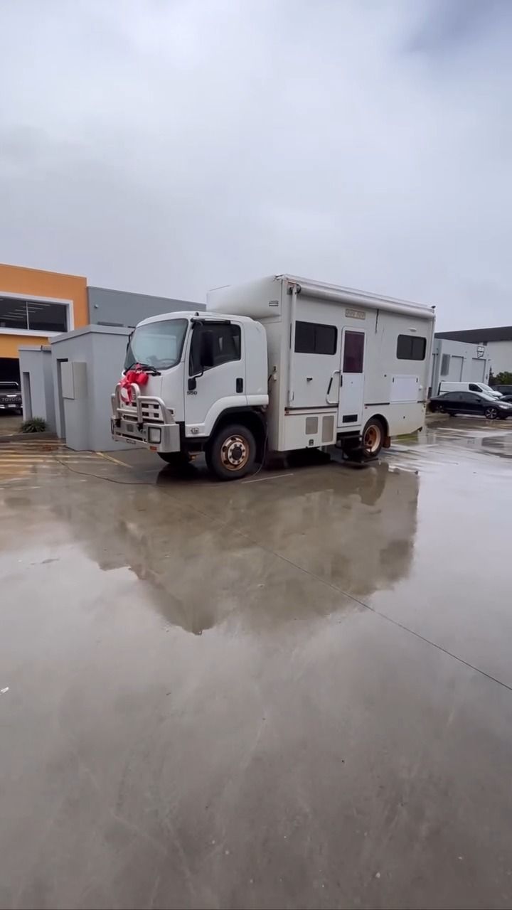 A White RV Is Parked In A Puddle Of Water In A Parking Lot — Live Unbound Campers In Upper Coomera, QLD