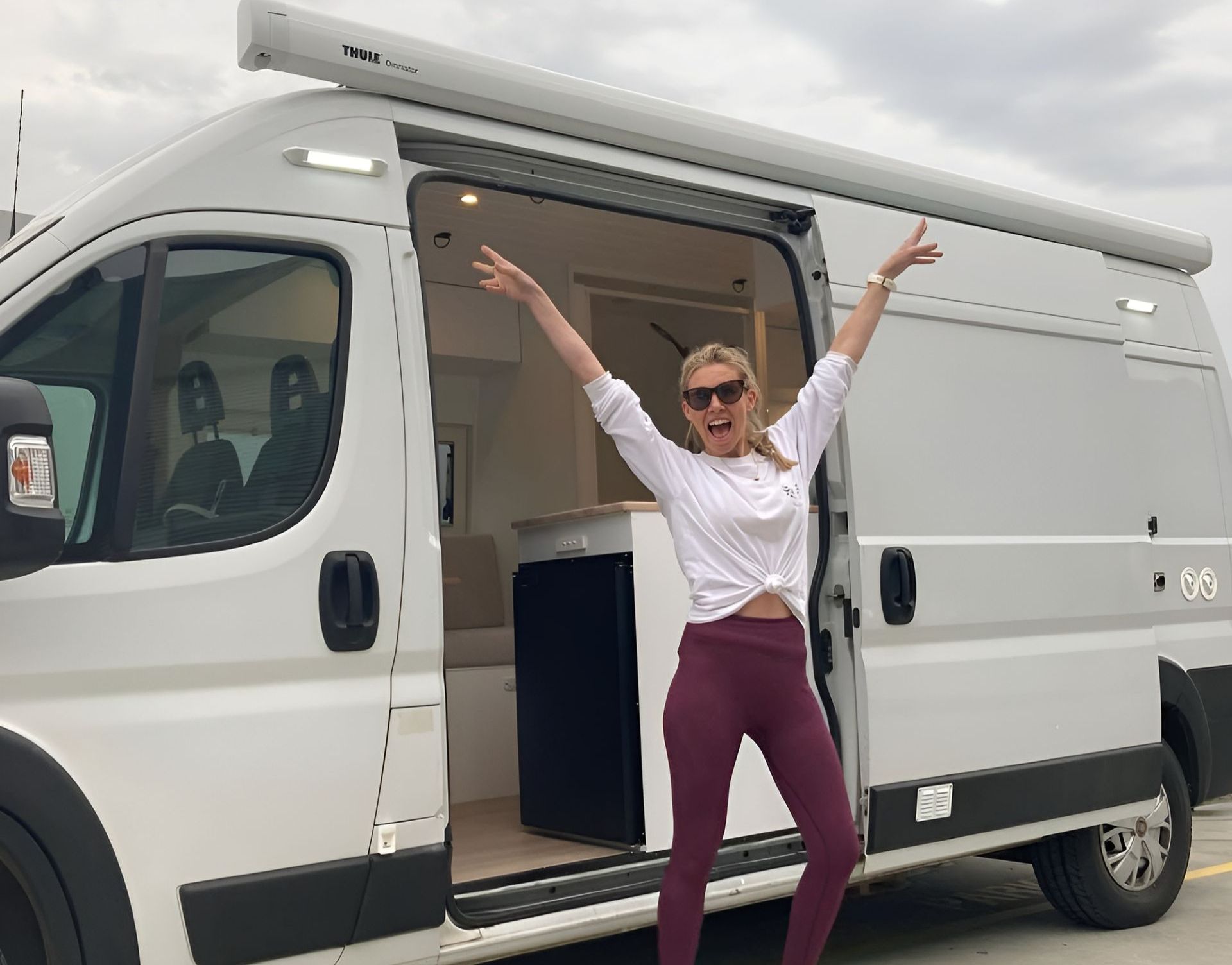 A Woman Is Standing In Front Of A White Van With Her Arms In The Air — Live Unbound Campers In Brisbane, QLD