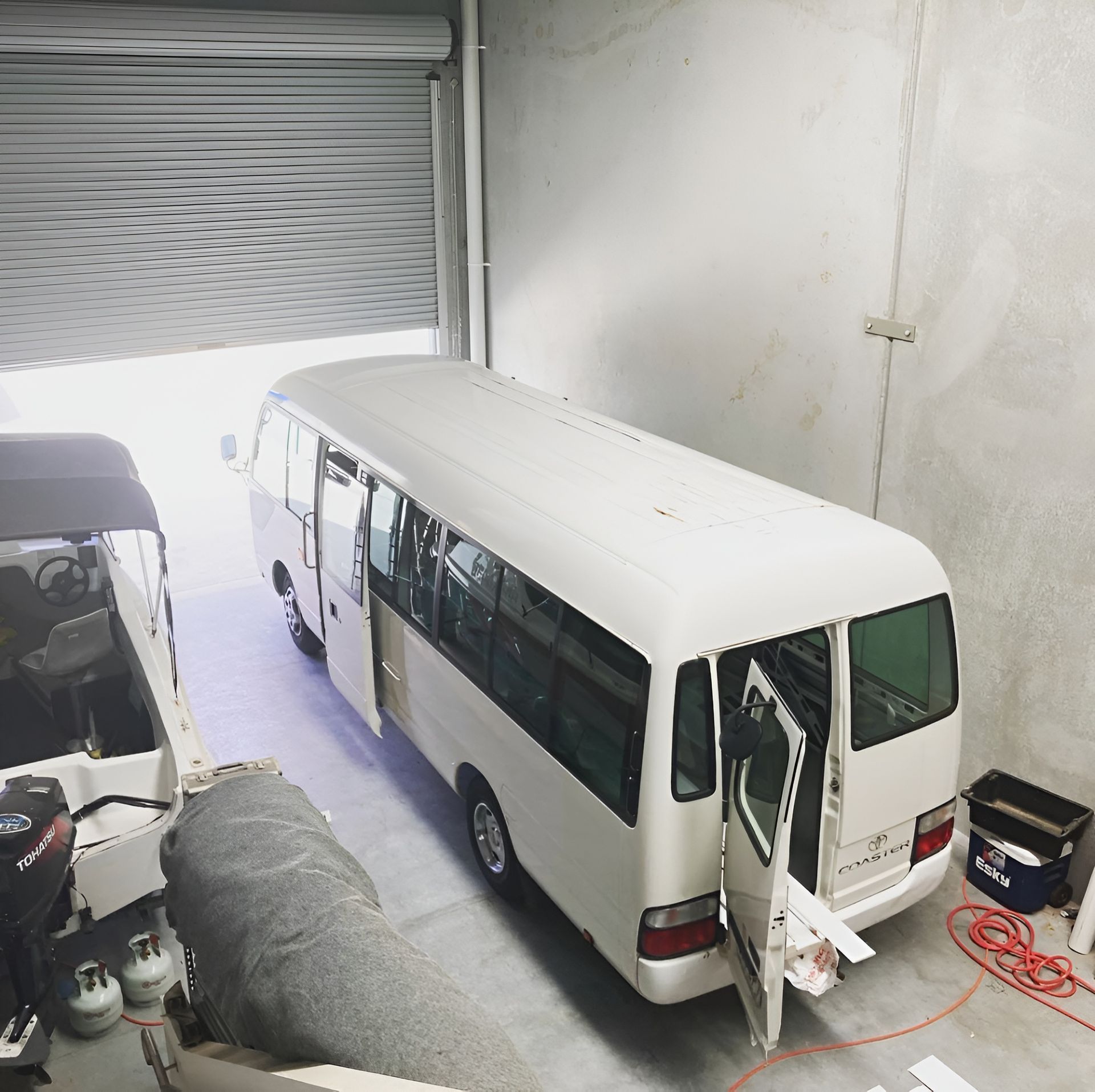 A White Bus Is Parked In A Garage With Its Doors Open — Live Unbound Campers In Gold Coast, QLD