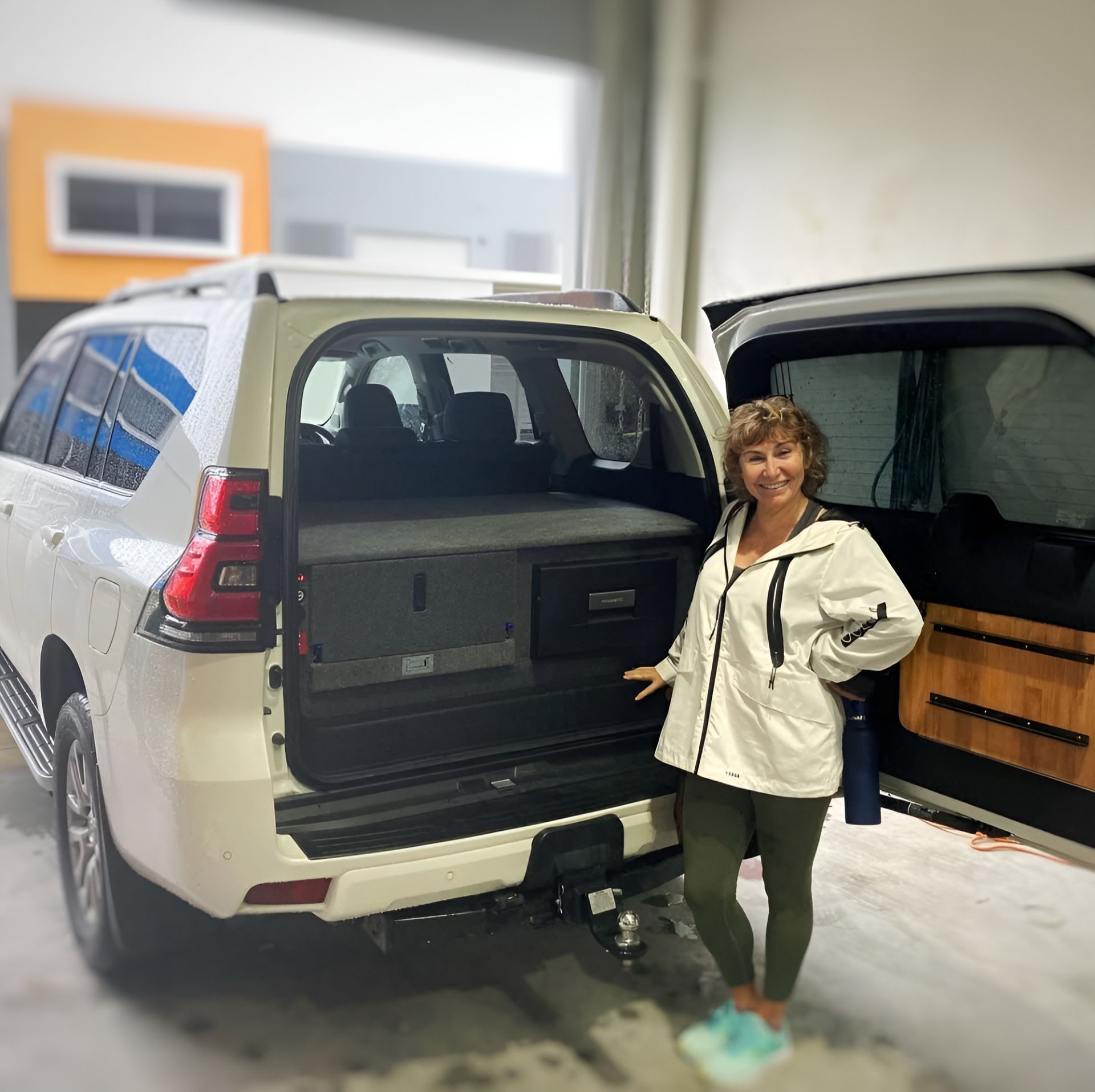 A Woman Is Standing In Front Of A White SUV With The Door Open — Live Unbound Campers In Tweed Heads, NSW