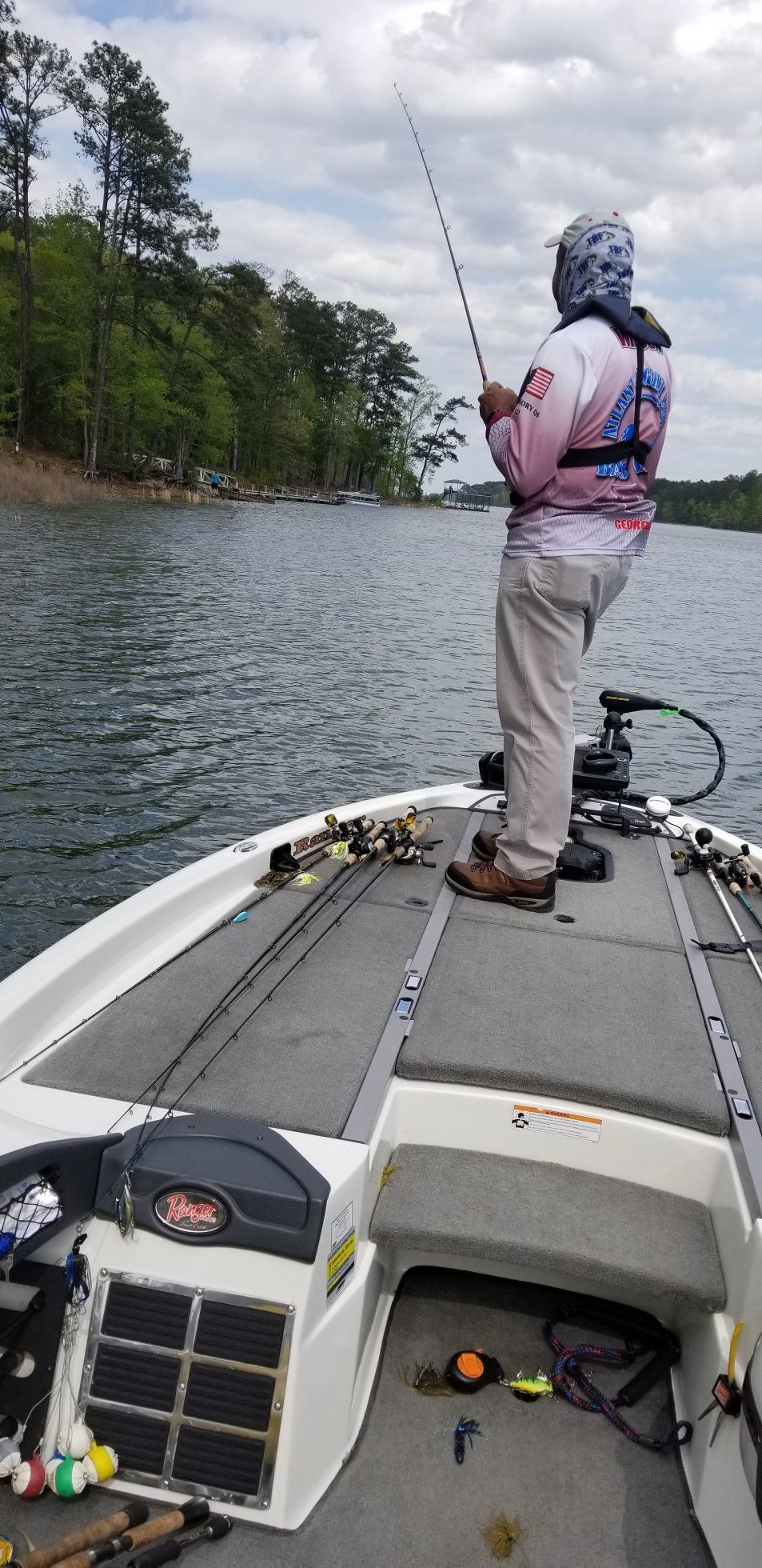 Person fishing from a boat on a lake, trees and cloudy sky in the background.