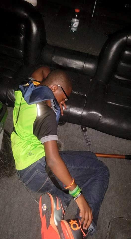 Man lying down on a dark floor next to an inflatable structure, wearing green shirt, jeans, and glasses.