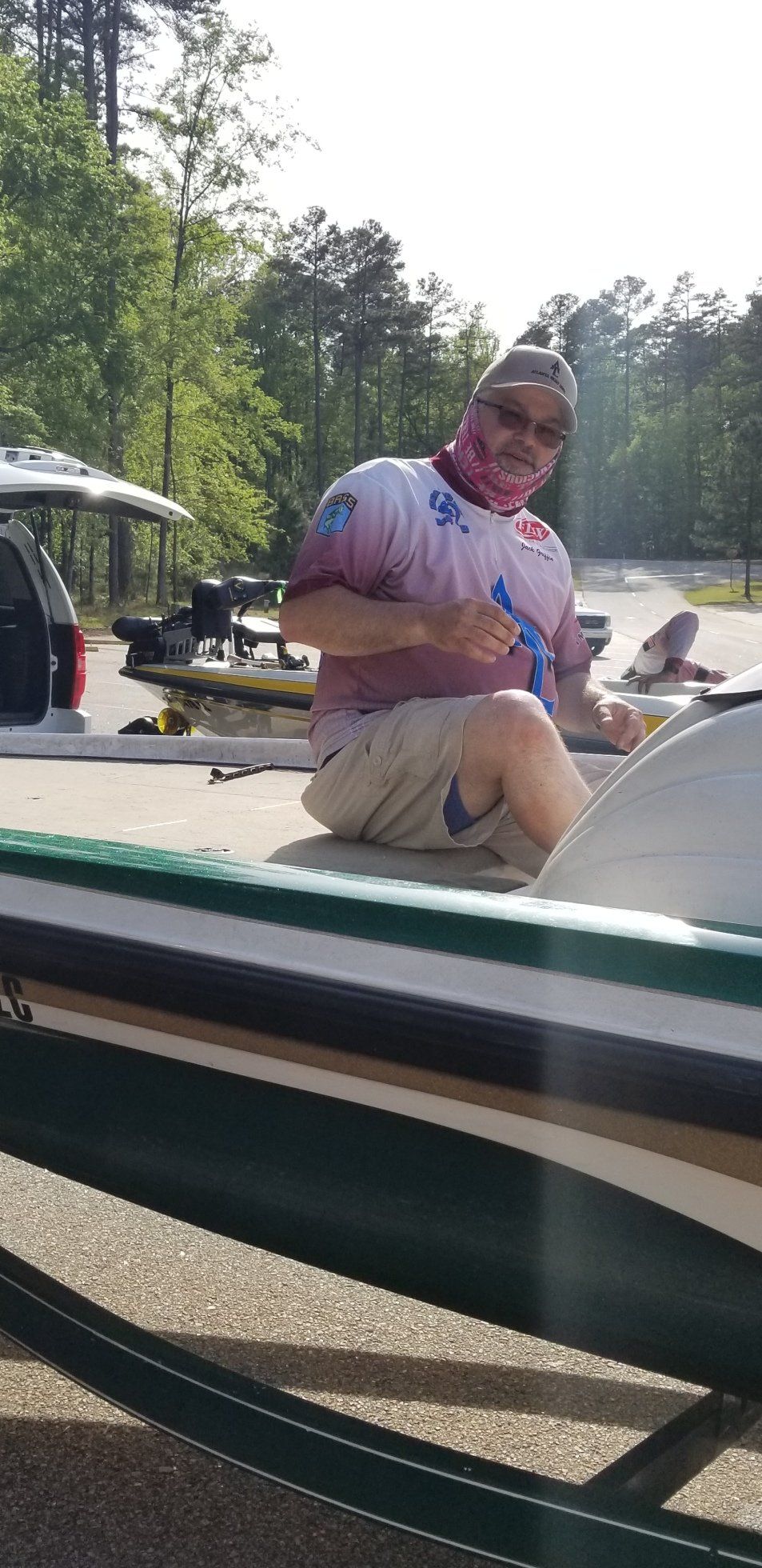 A man in a boat, wearing sunglasses and a pink face covering, at a boat ramp.