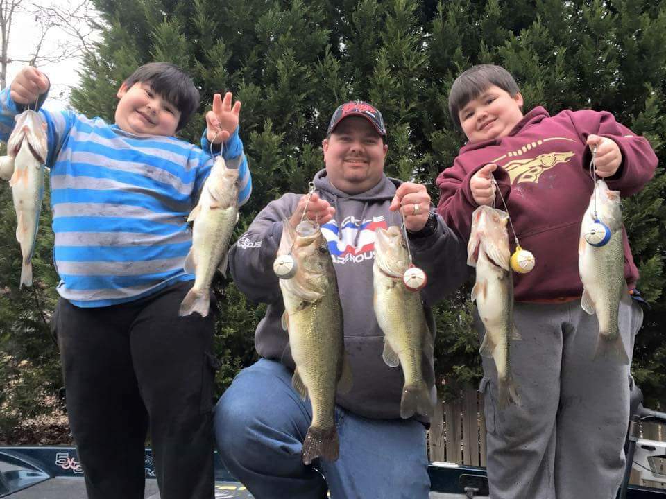 Three people, two boys and a man, holding up bass they caught on a boat.