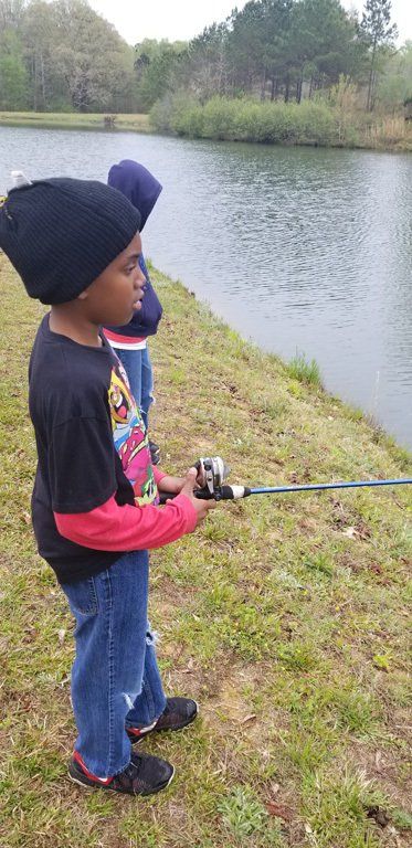 Two young boys fishing at a lake; one holds a fishing rod.