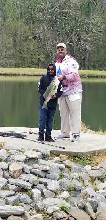 Person and child holding a large fish on a dock by a lake.