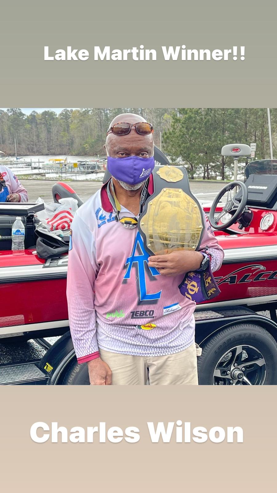 Charles Wilson holding a championship belt, Lake Martin winner, standing in front of a boat, wearing a mask.