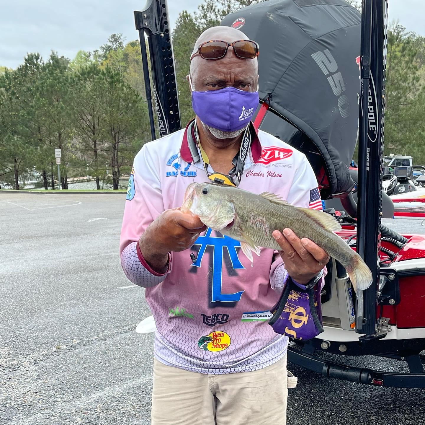Man in fishing gear holding a fish, near a boat, wearing a mask.