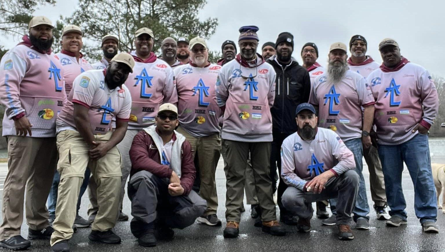Group of men in matching pink shirts by water, some with beards.