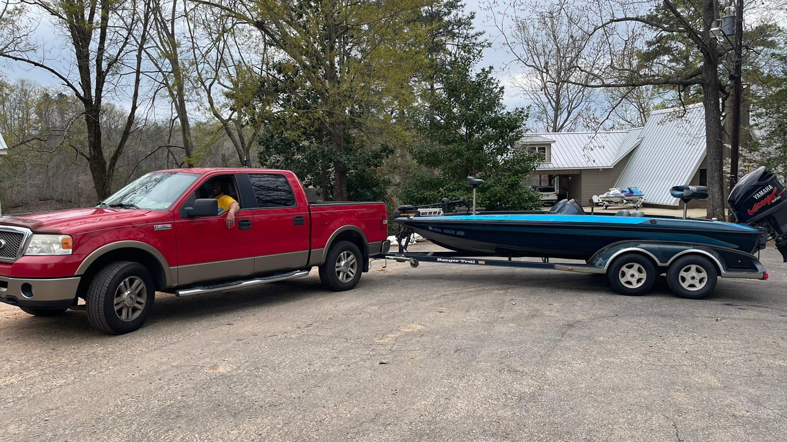 Red truck towing a blue boat on a trailer in front of a house.