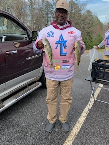 Man in fishing gear holding two fish next to a truck.