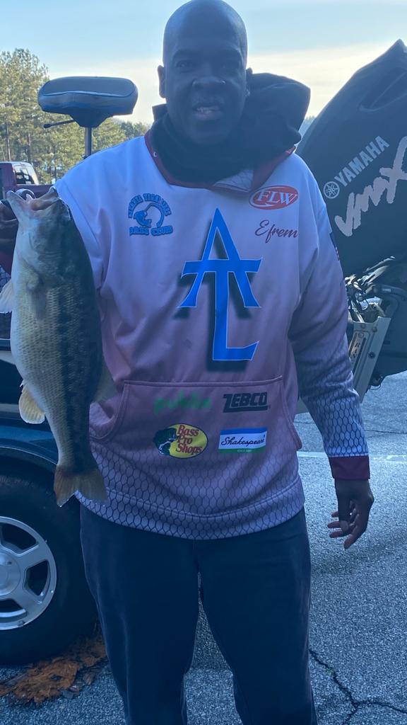 Man in pink hoodie holding a largemouth bass on a boat dock.
