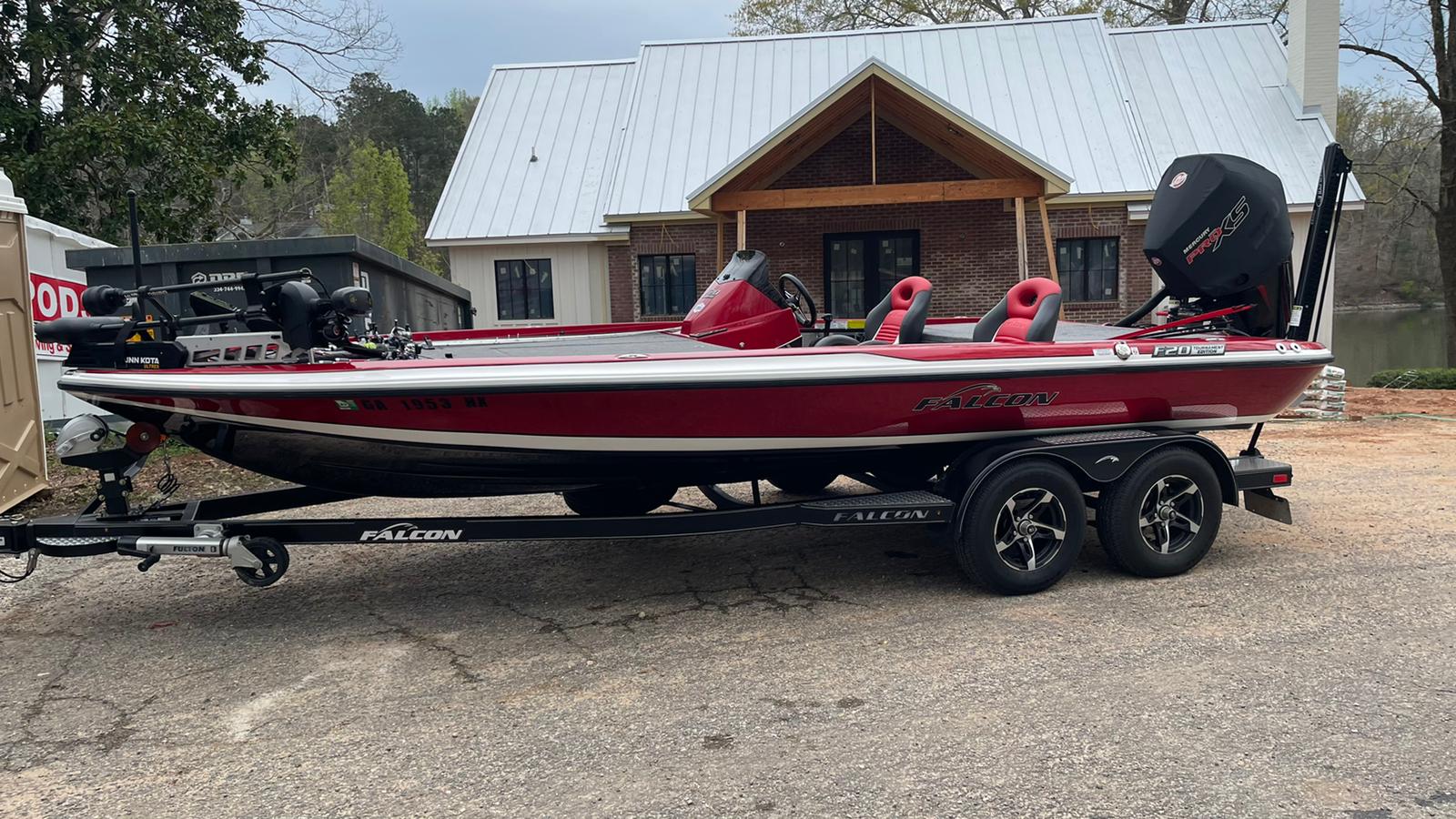 Red and white bass boat on a trailer parked in front of a house with a lake visible in the background.