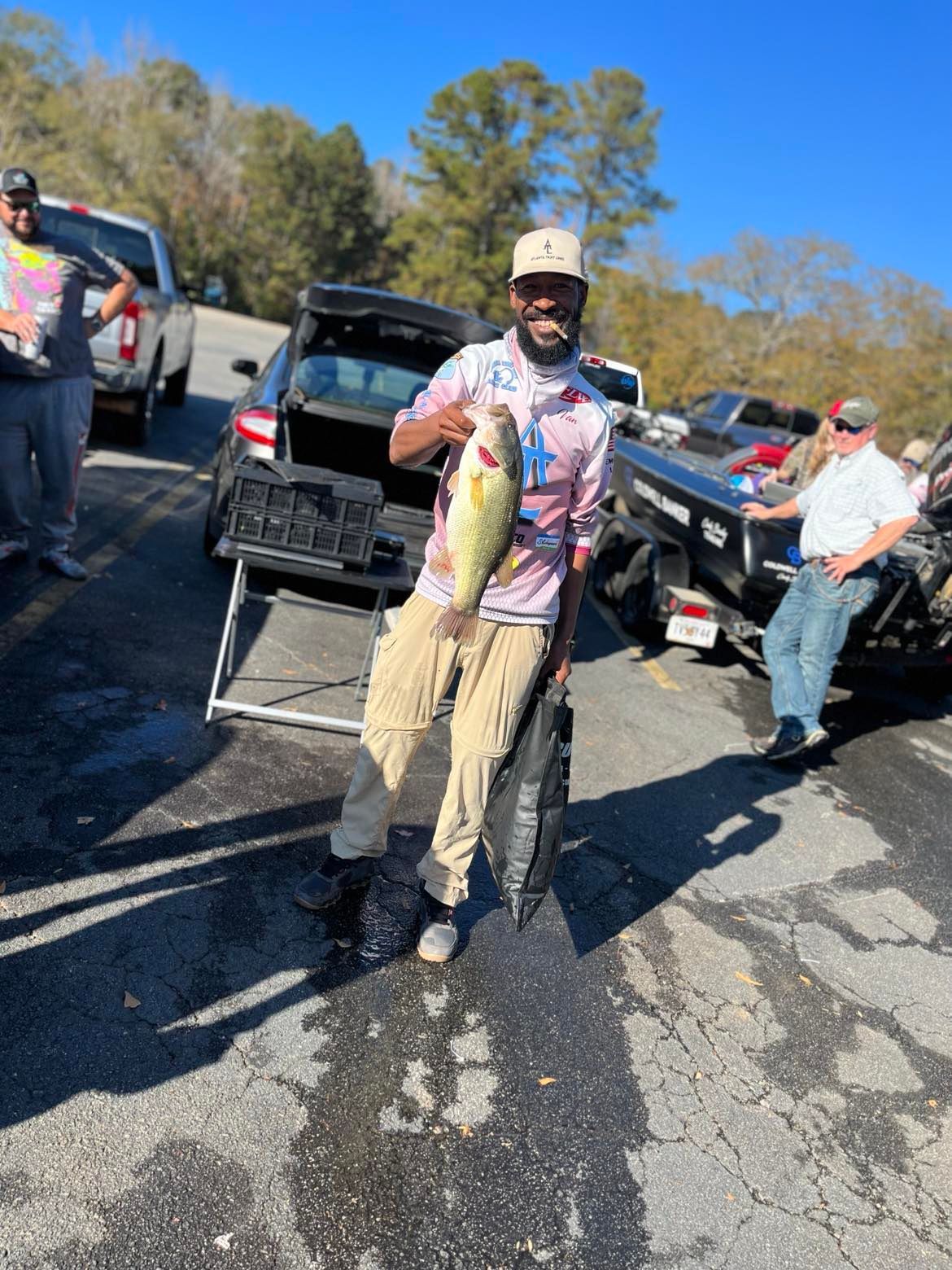 Man holding a large fish at a boat ramp, standing next to a car with others present.