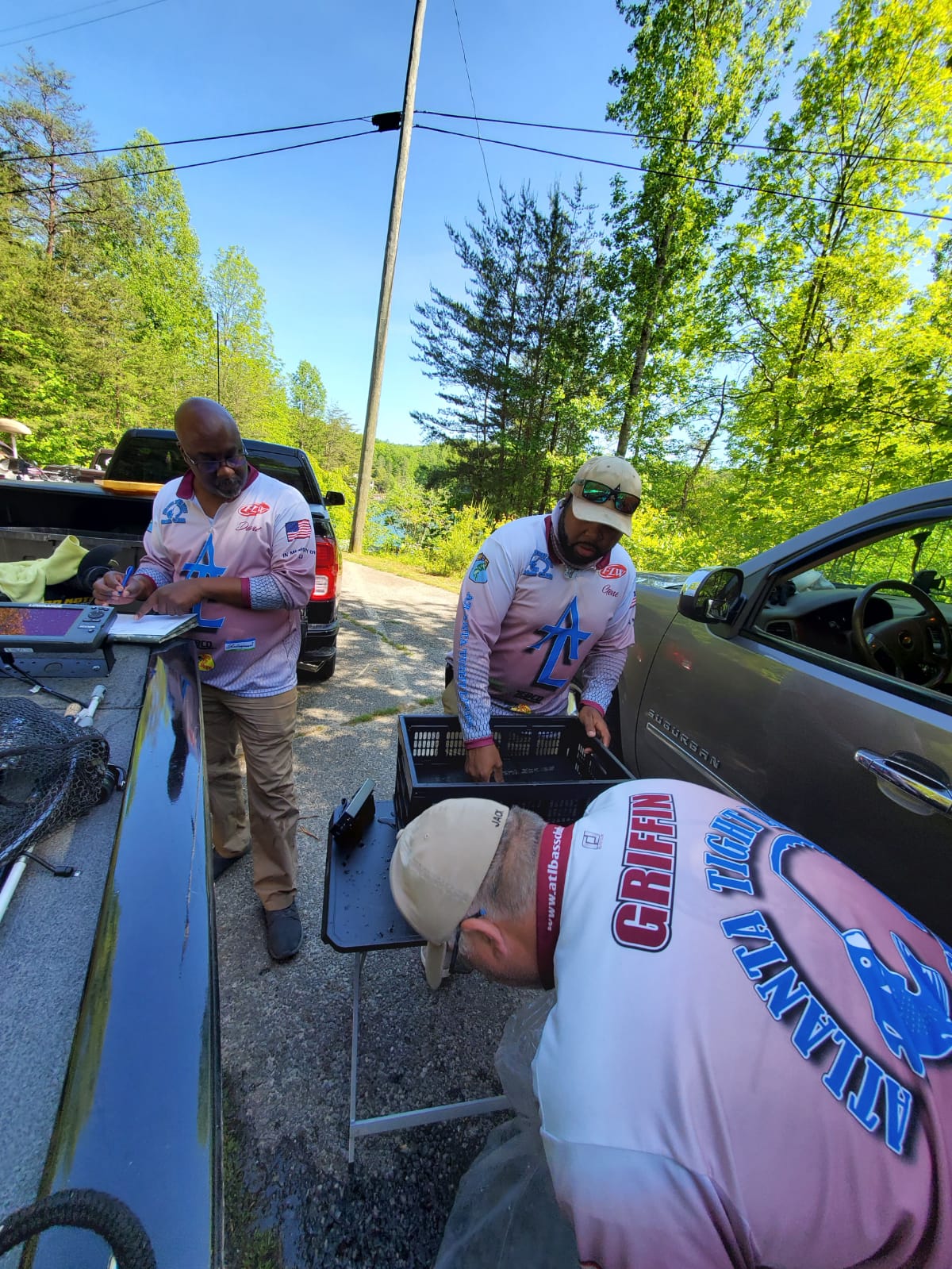 Three men in matching pink shirts weigh fish at a boat ramp.