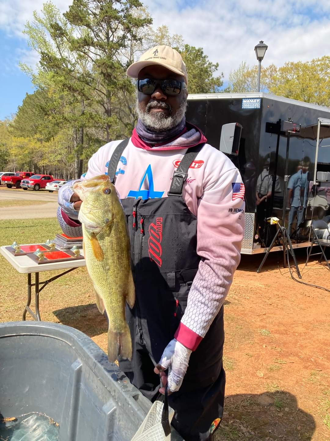 Man in waders holding a large bass at a lakeside event.