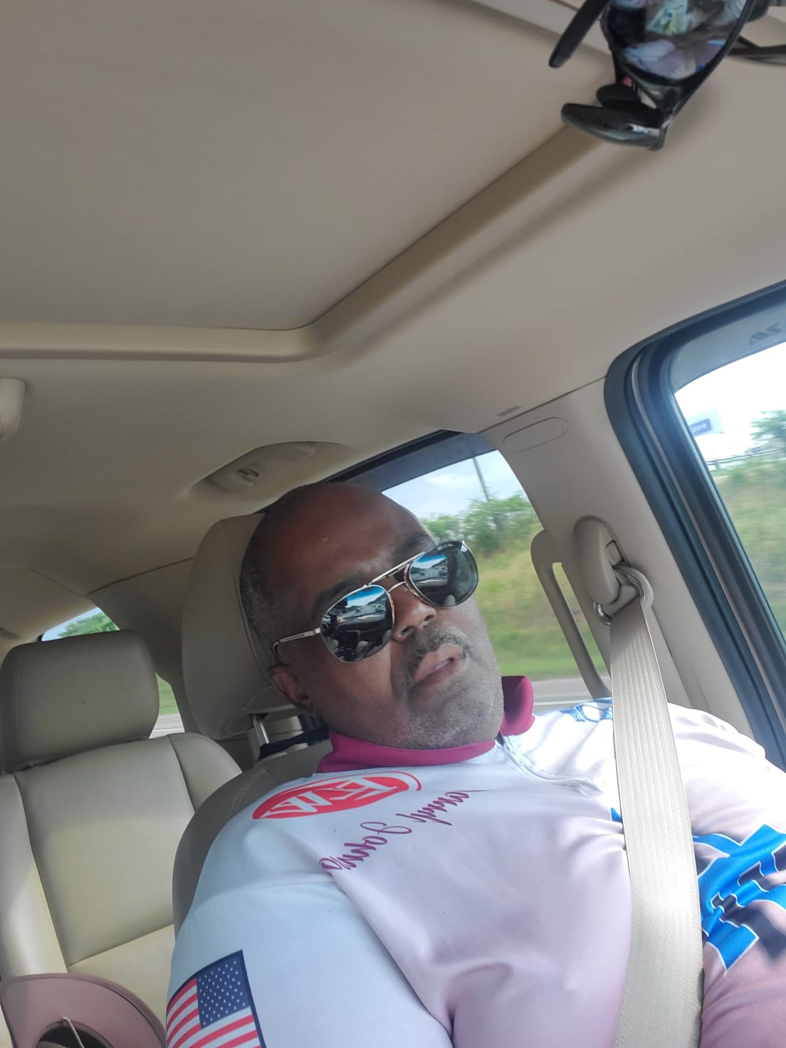Man in sunglasses in car, looking tired. American flag on shirt.