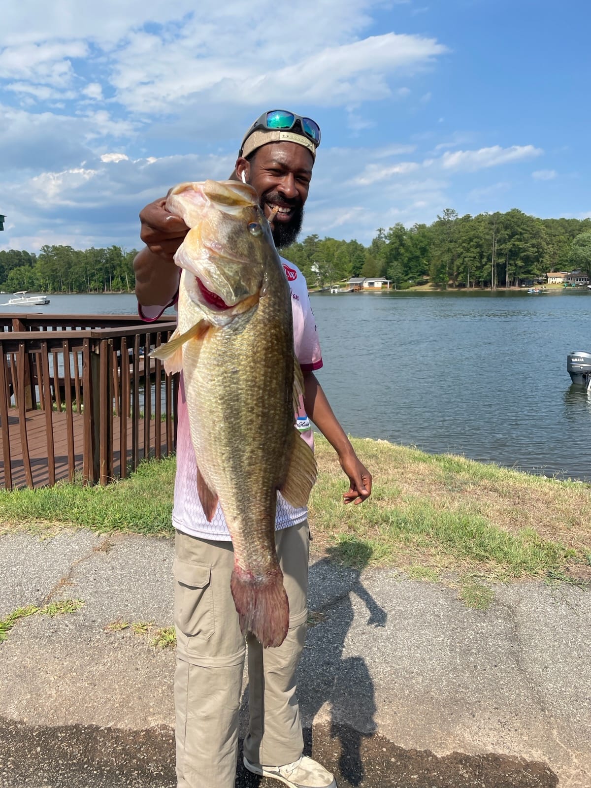 Man holding a large bass fish near a lake, smiling.