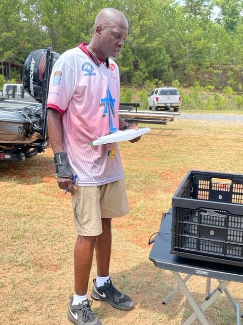 Man in pink shirt standing outside, holding a white plate and looking at a black crate.