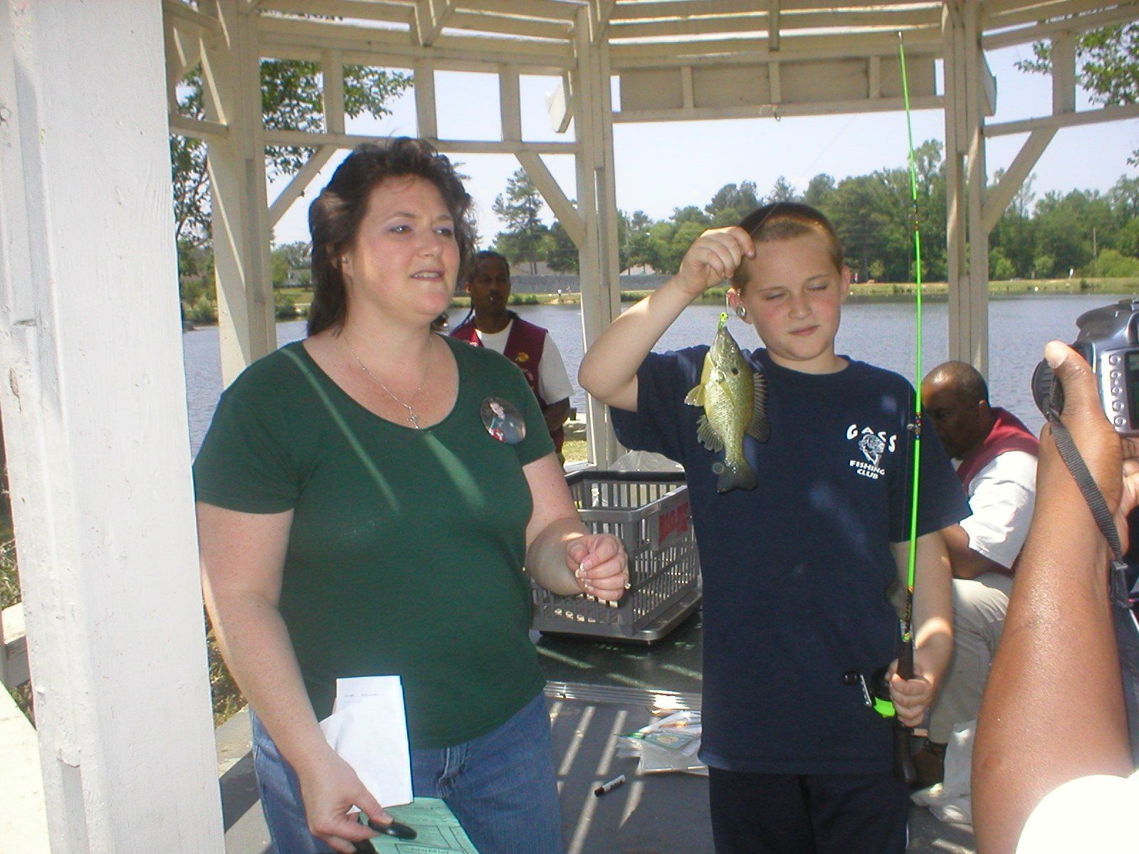 Woman and boy in gazebo with a fish. Boy holds up fish, smiling. Others watch.