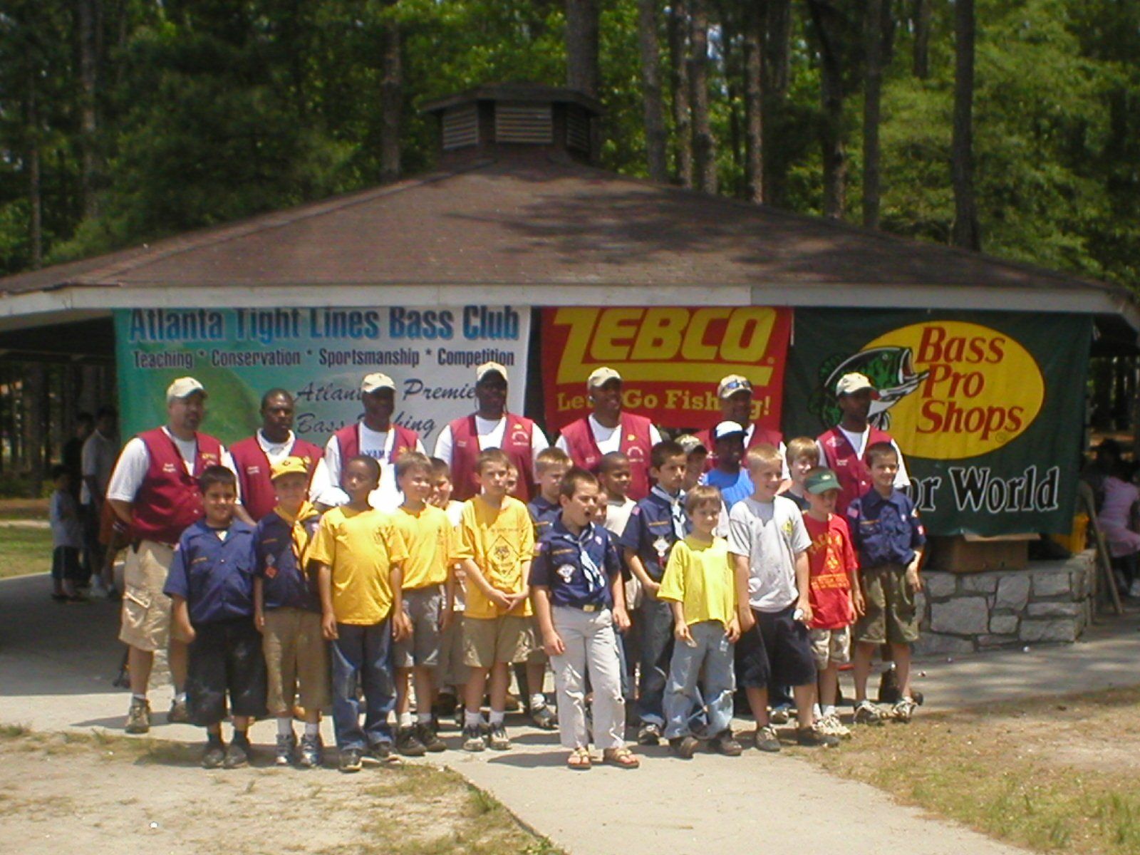 A group of children and adults in front of a pavilion, possibly at a fishing event.