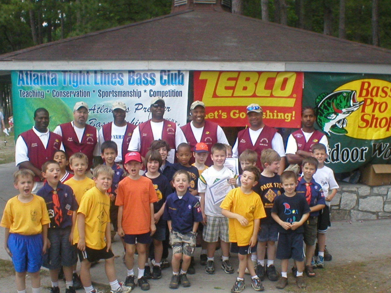 Group of kids and adults posing near a Bass Pro Shop banner.