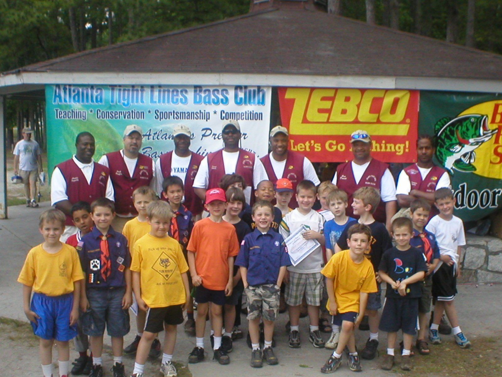 Group photo: Atlanta Tight Lines Bass Club members and young boys in front of a fishing booth.