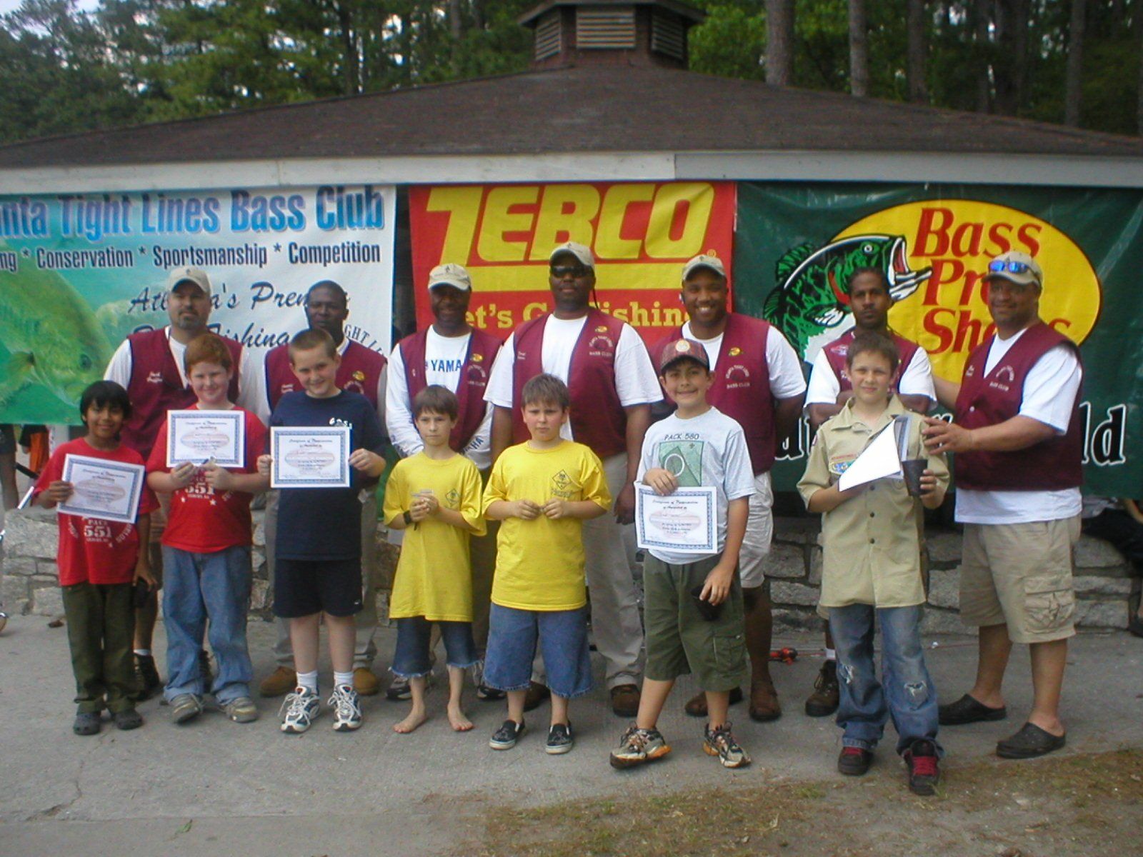 Youth fishing club members with awards and mentors, outdoors.