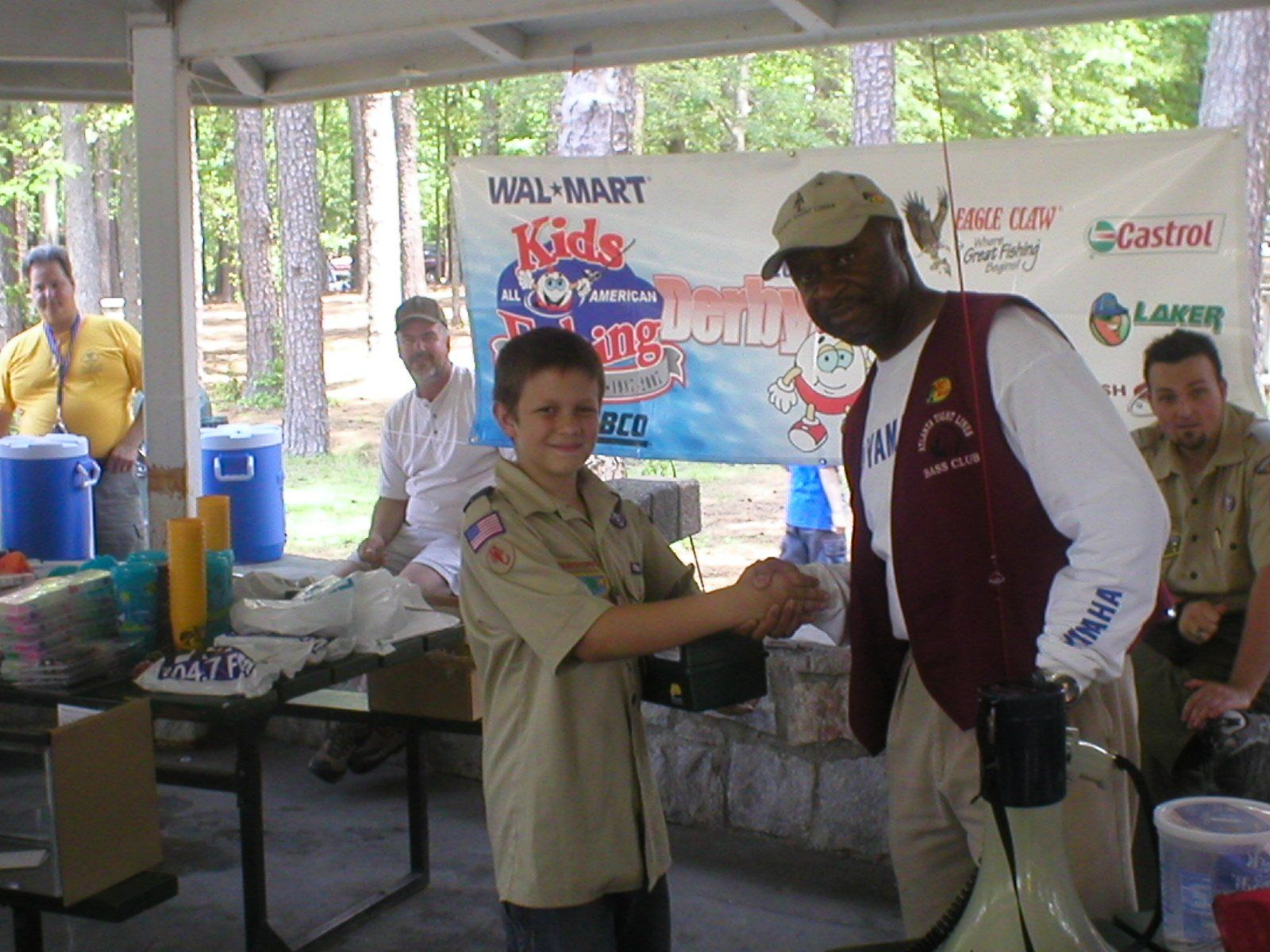 Boy Scout shaking hands with an older man at a Walmart Kids fishing event.