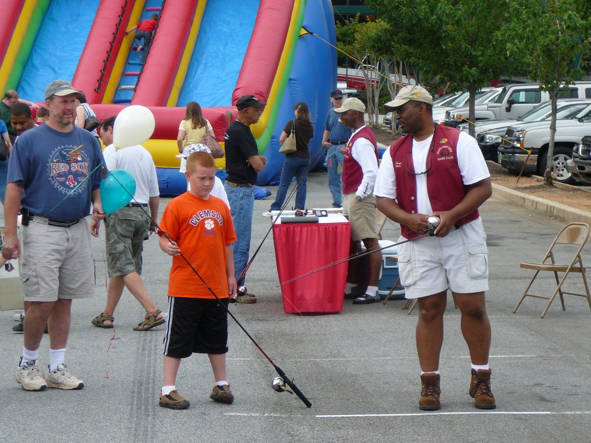 People fishing at an outdoor event near an inflatable slide and cars.