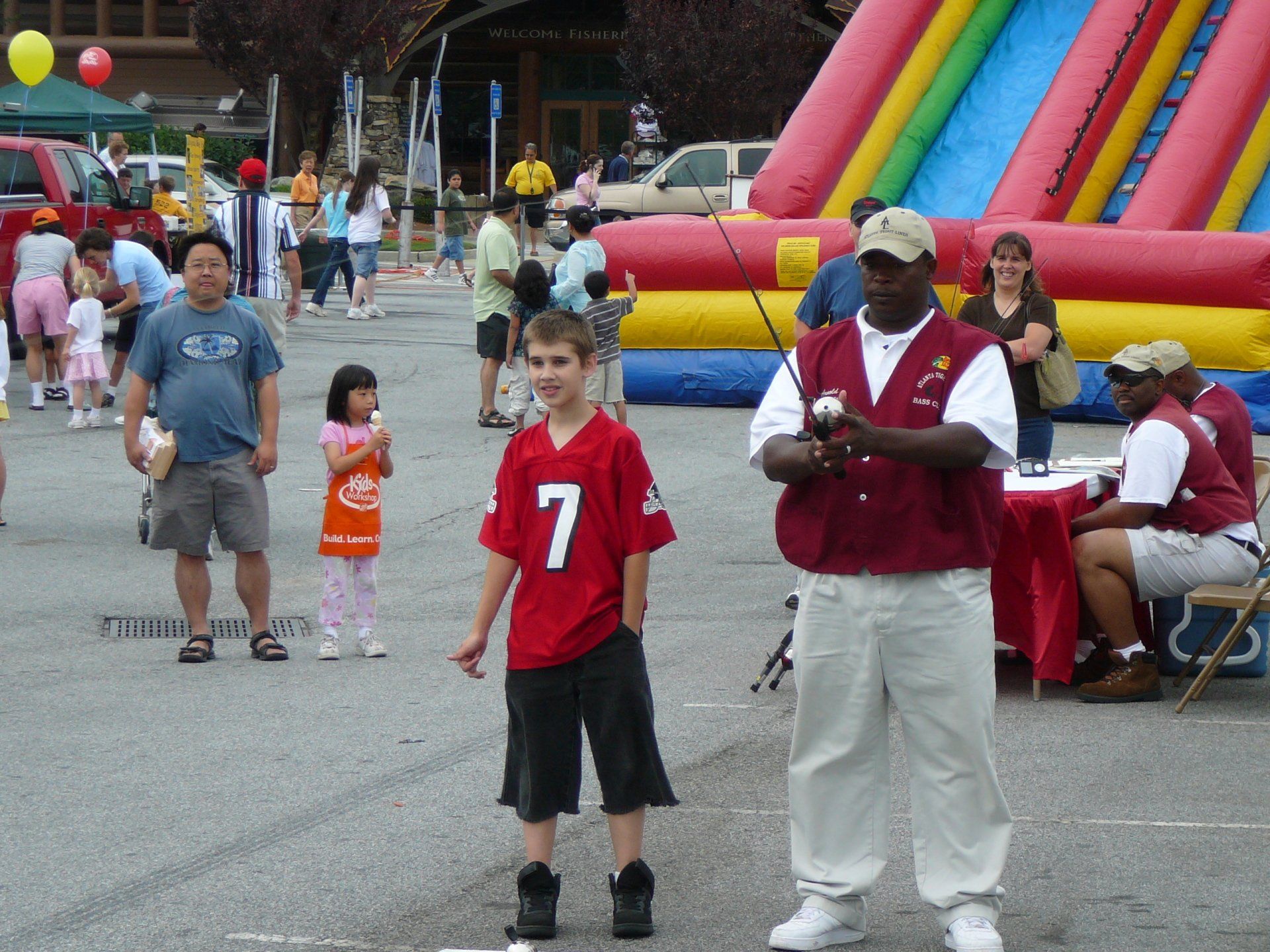 Community event with people, a boy fishing with an instructor, and an inflatable slide.
