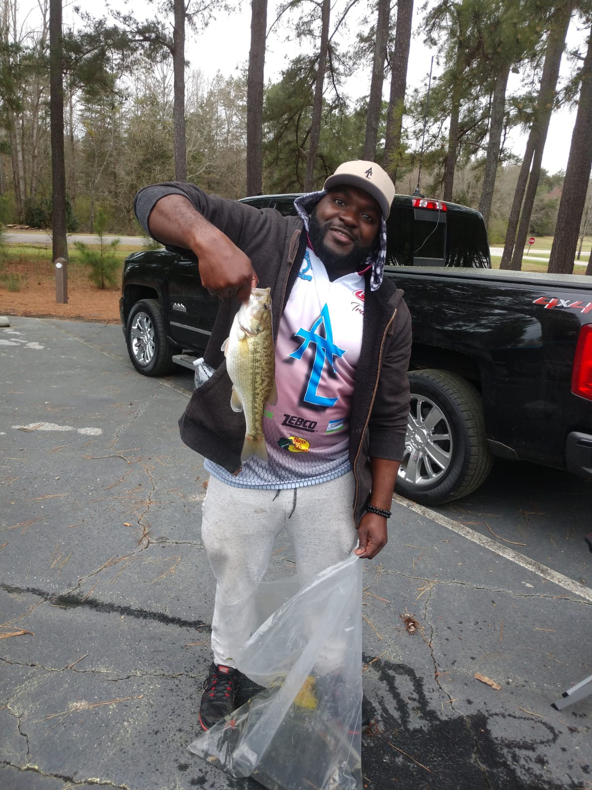 Man holding a fish, smiling, near a black truck in an outdoor setting.