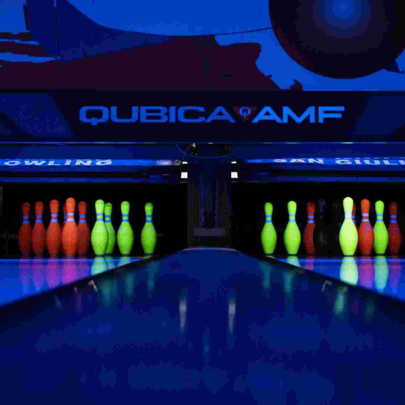 Pista da bowling fosforescente con birilli e piste al neon, insegna QubicaAMF.