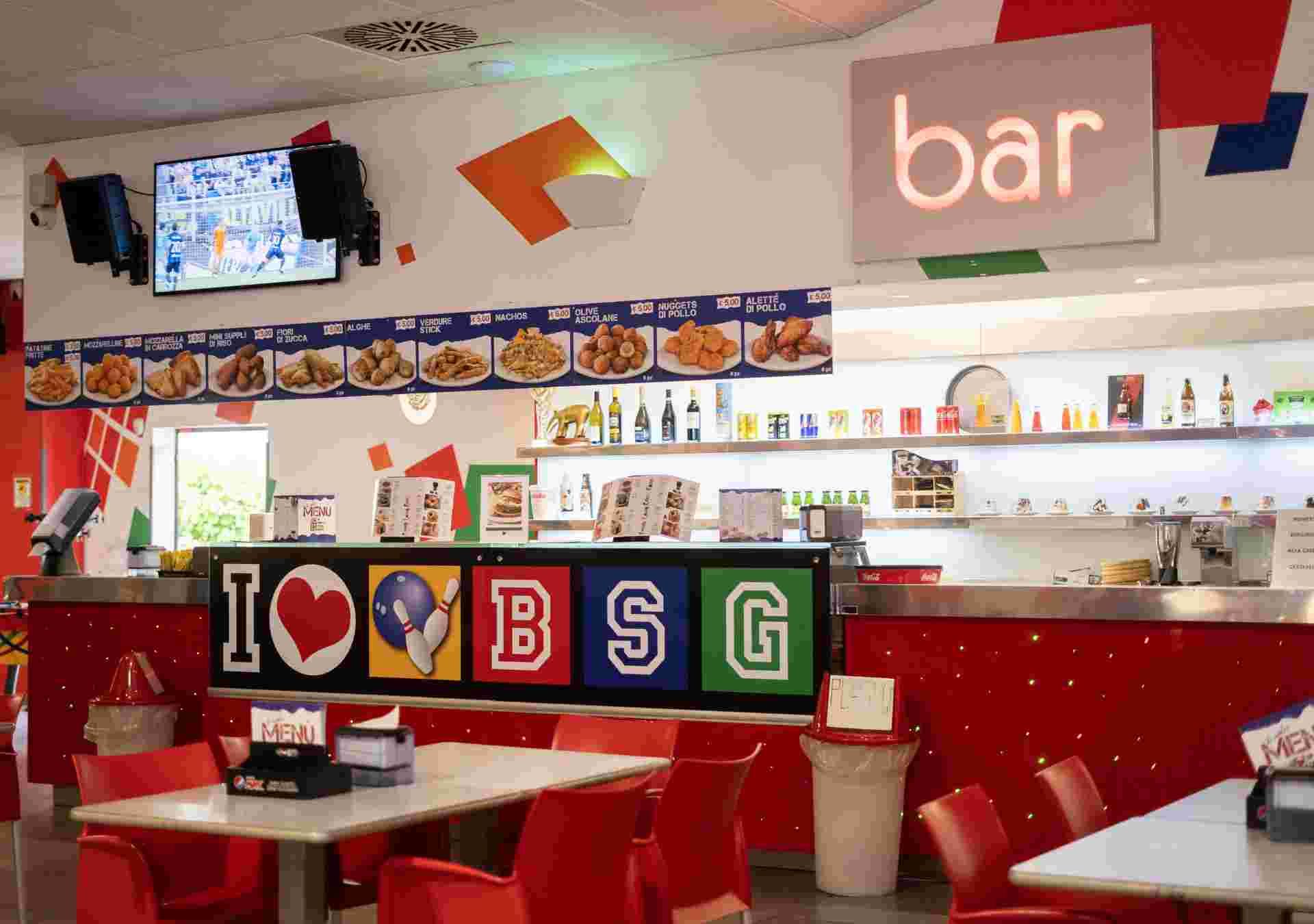 Interno di un bar dai colori vivaci con TV, menù, bancone e tavoli. Arredamento con la scritta 