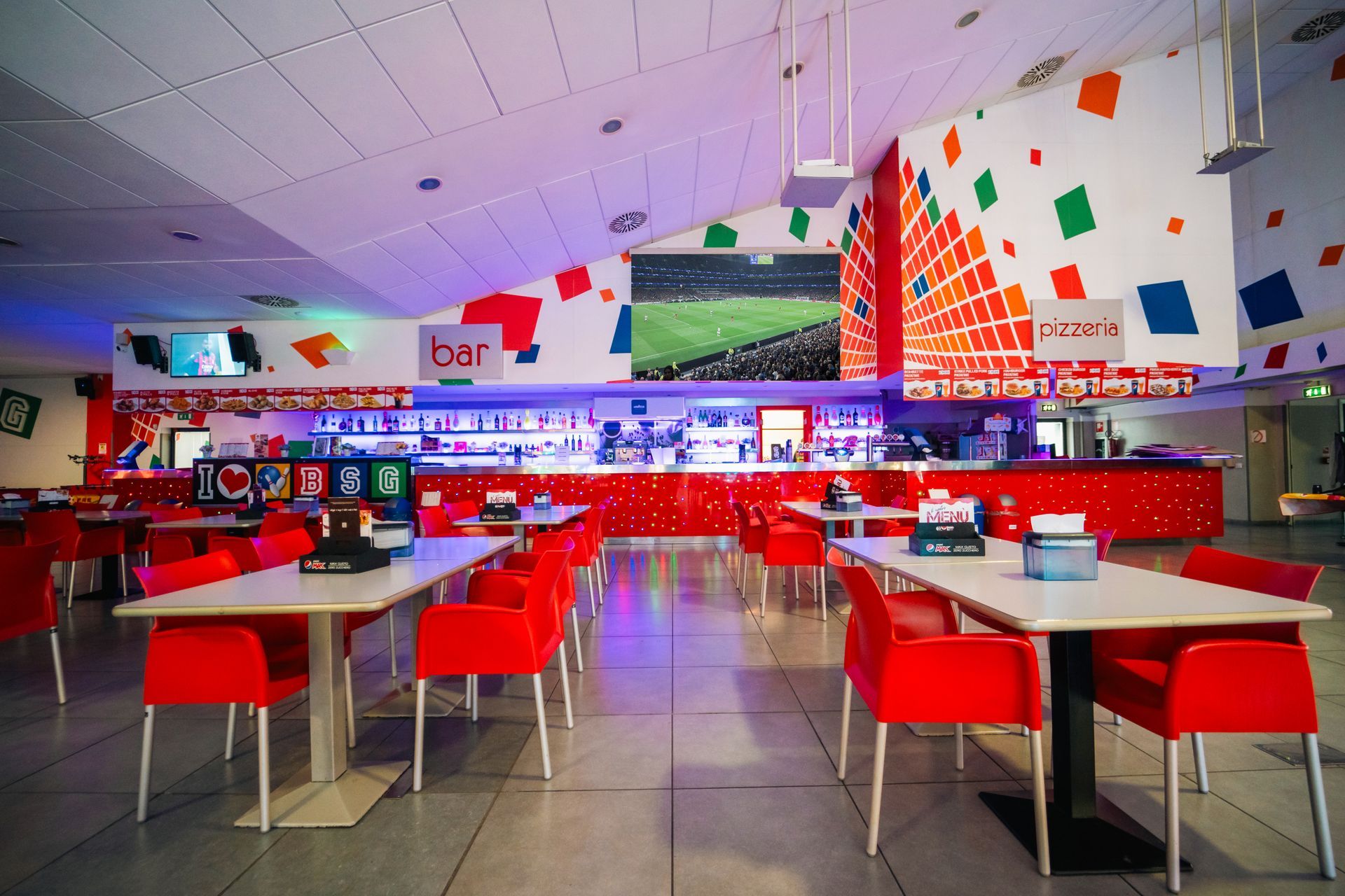 Interno di un bar con tavoli e sedie rossi, un'insegna 