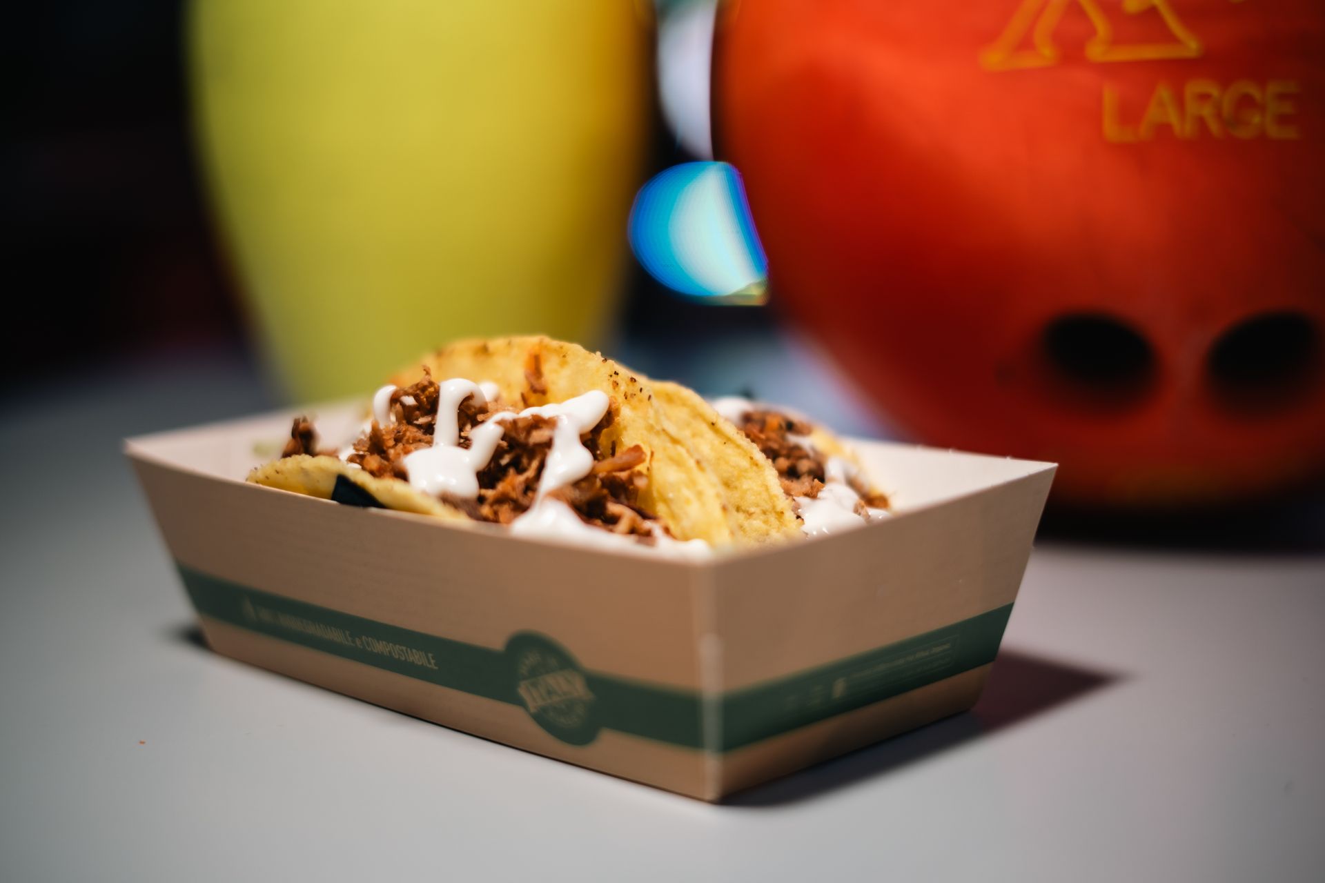 Palla da bowling rosa, boccale di birra e pizza su una tavola di legno in una pista da bowling.