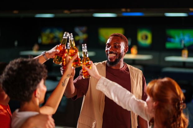 Persone in un bar scarsamente illuminato che brindano con bottiglie di birra. Una persona sorridente è il soggetto centrale.