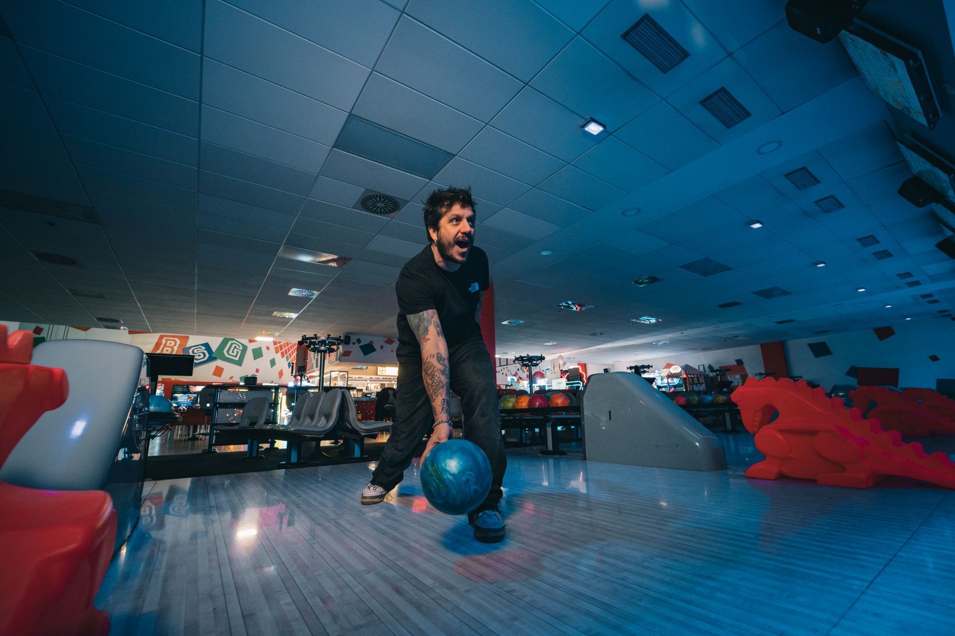 Interno di una pista da bowling con più corsie, aree salotto e schermi sopra le corsie.