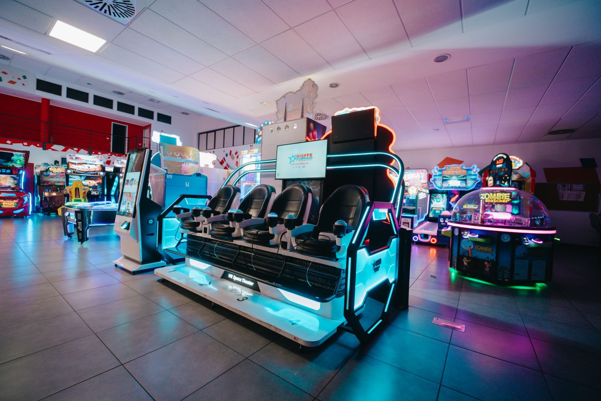 Interno di una pista da bowling con piste, posti a sedere, tavoli e schermi. Combinazione di colori arancione e blu.