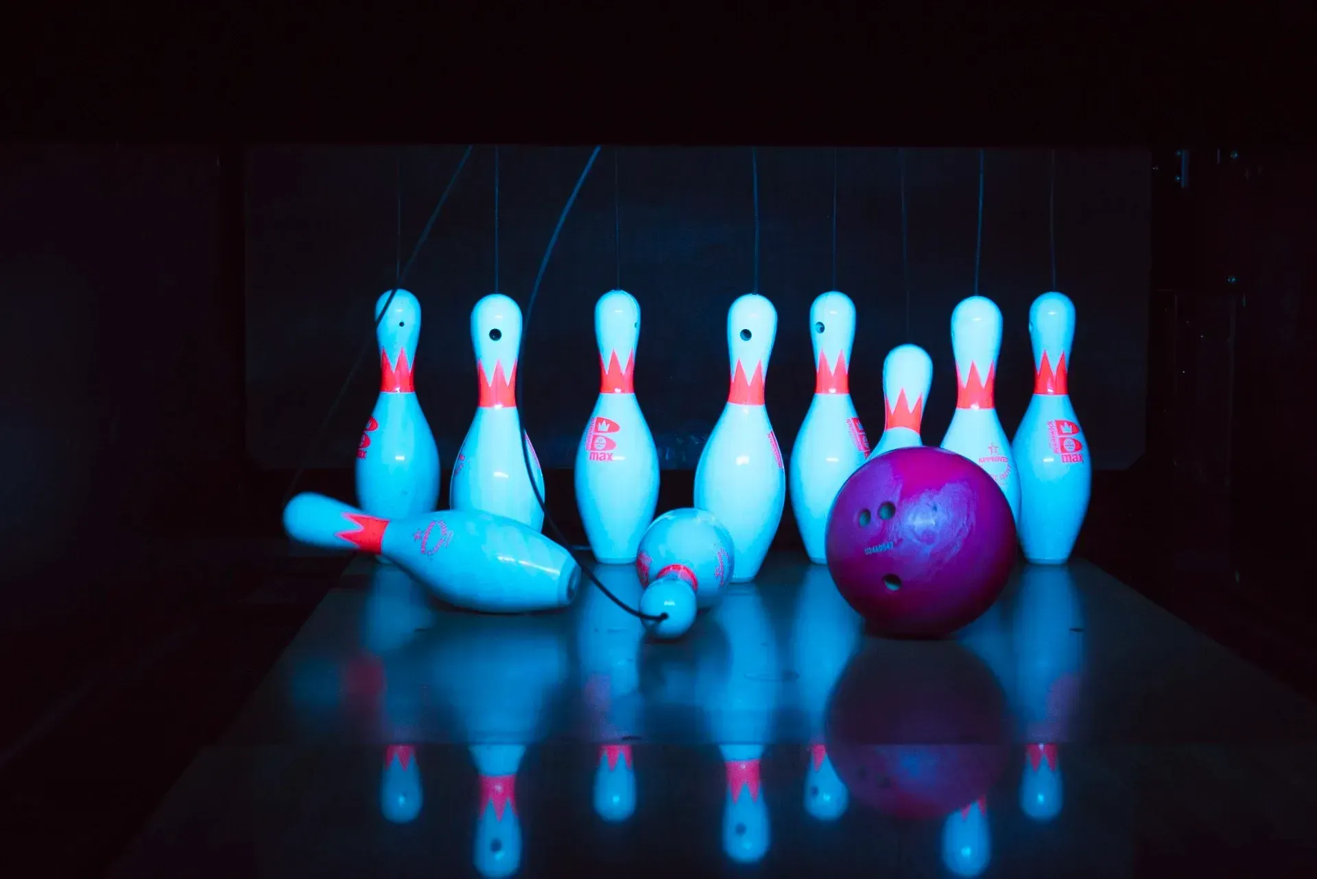 Birilli e palla su una pista lucida, alcuni birilli abbattuti, palla viola, illuminazione blu.