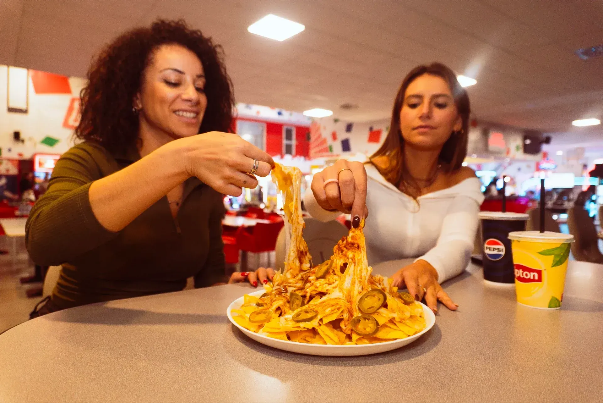 Due donne che servono nachos al formaggio seduti a un tavolo in una pista di pattinaggio illuminata.