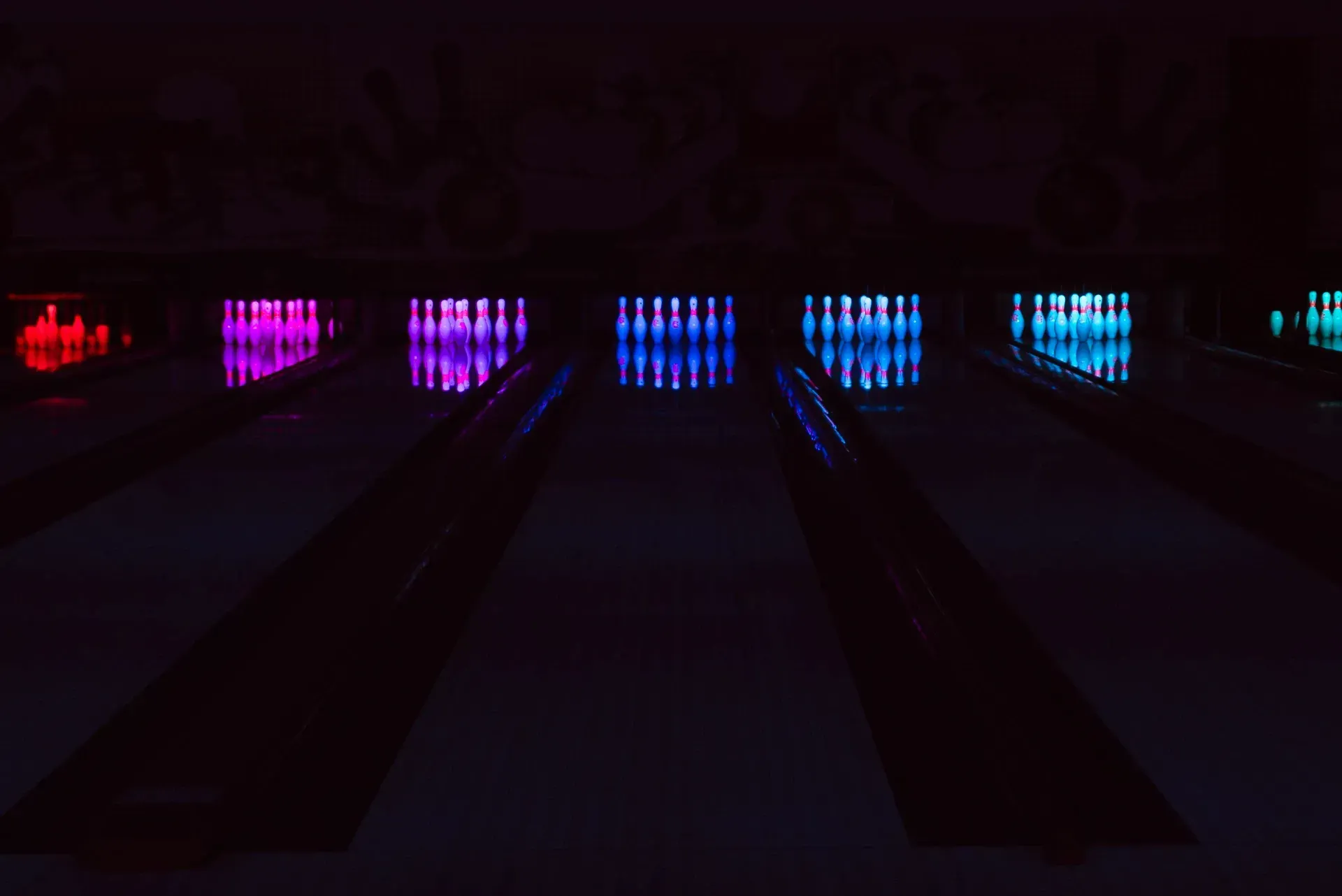 Le piste da bowling sono illuminate da luci di diversi colori che si riflettono sui birilli in una stanza buia.