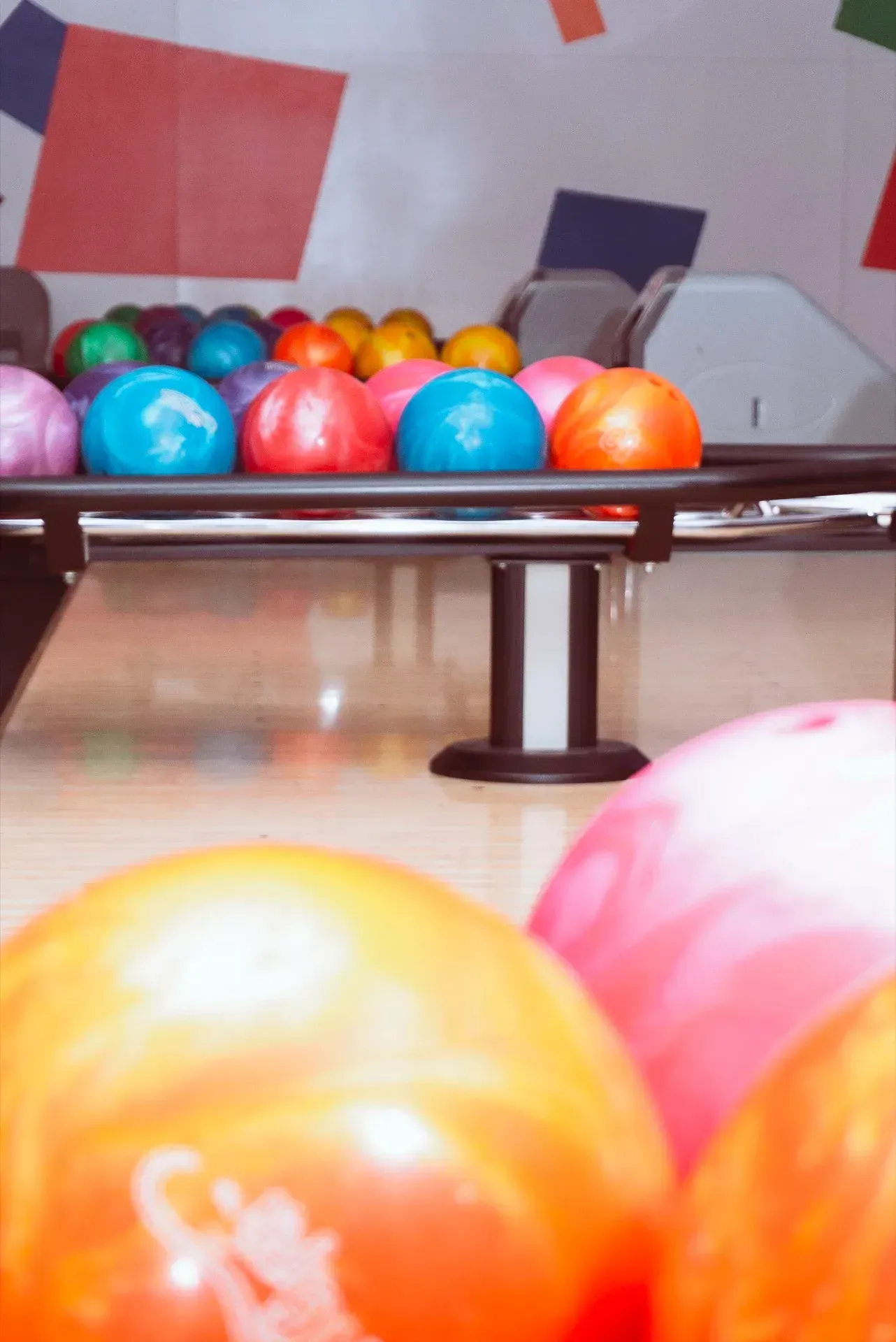 Palle da bowling di vari colori su un supporto, pista sullo sfondo.
