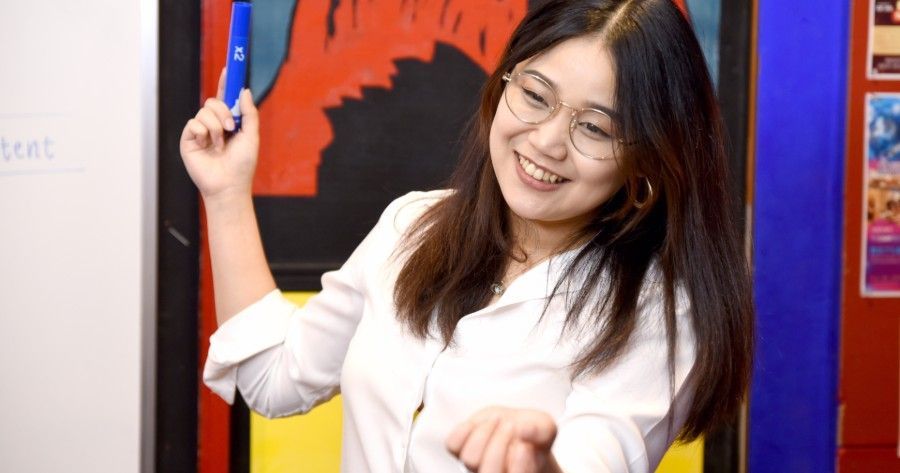 Smiling person in a white shirt posing with raised arms in front of a colorful mural