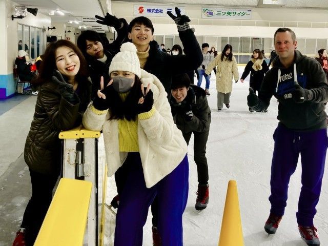 Group of people pose on an ice rink. Some smile, wave, and make peace signs.