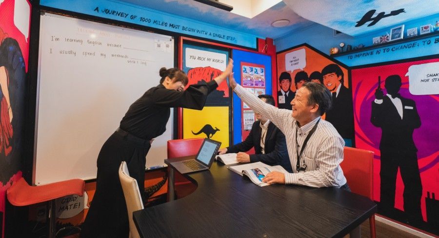 Two people high-fiving in a colorful room. A person sits at a table with a laptop and papers. Background includes drawings.