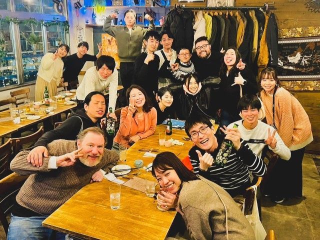 Group of people smiling at a table in a dimly lit restaurant. Some are making peace signs.