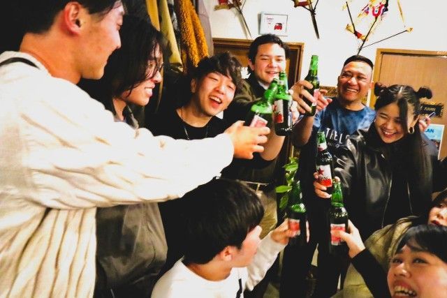 Group of people cheering with beer bottles in an indoor setting.
